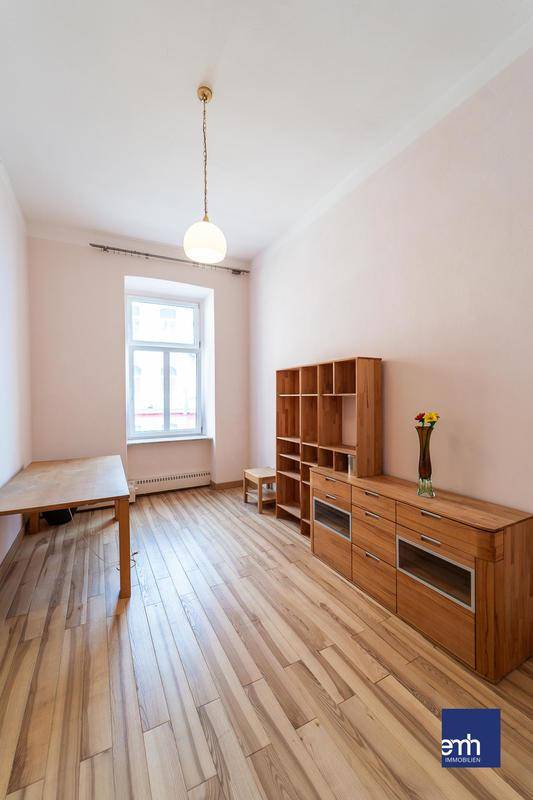 Helles Zimmer mit Holzboden, Holzregalen und einem großen Fenster.