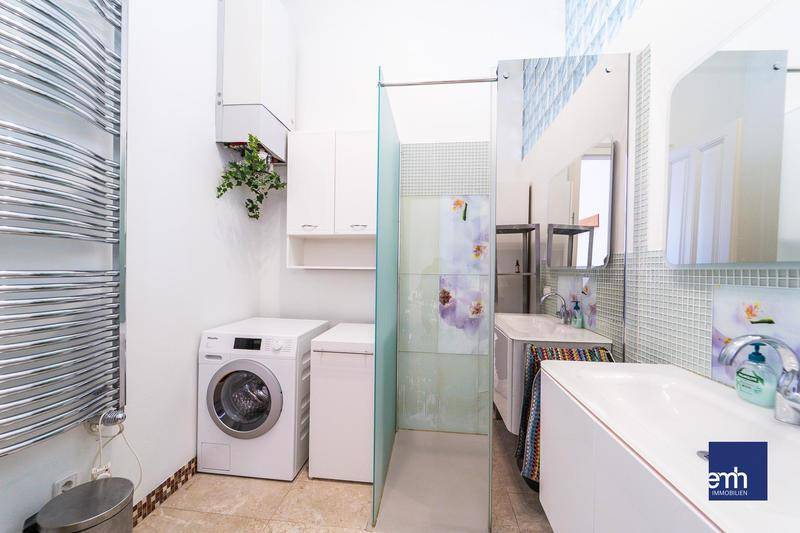 Modernes Badezimmer mit Dusche, Waschmaschine, Handtuchheizkörper und Mosaikfliesen.