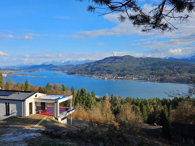 Modernes Haus mit Terrasse und weitem Blick auf den See und die schneebedeckten Berge.