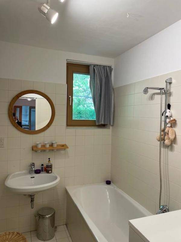 Badezimmer mit Badewanne, Waschbecken, Spiegel und einem Fenster für Tageslicht.