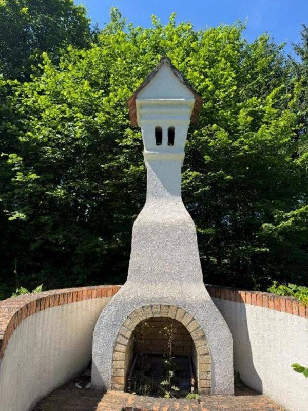 Gemauerter Grillplatz oder Außenkamin mit Ziegelmauer und umgebenden Bäumen im Gartenbereich.