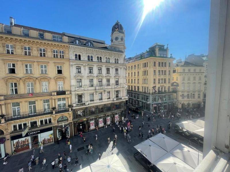 Sonniger Ausblick auf einen historischen Stadtplatz mit architektonisch vielfältigen Gebäuden und vielen Menschen.