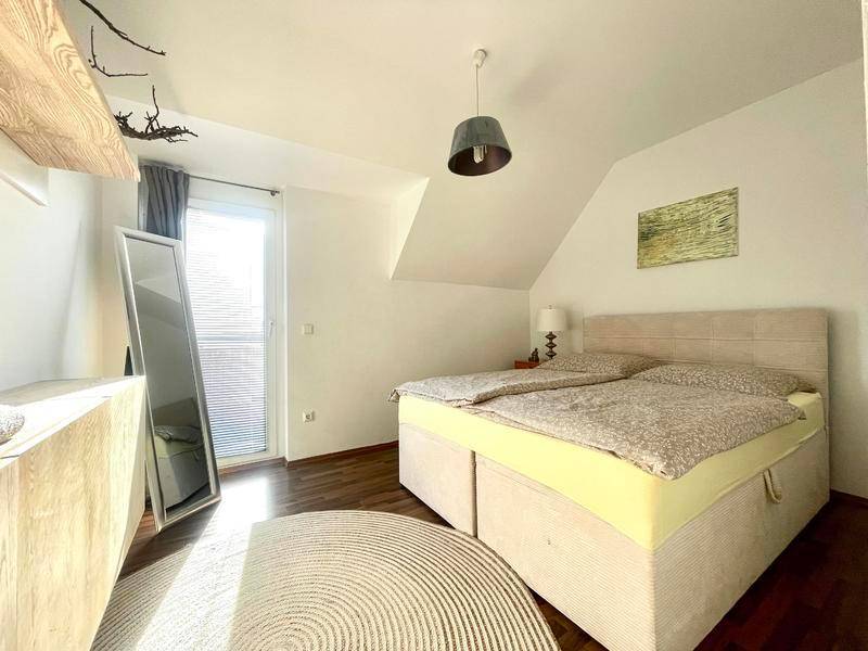 Schlafzimmer mit Doppelbett, dunklem Holzboden und Zugang zum Balkon.