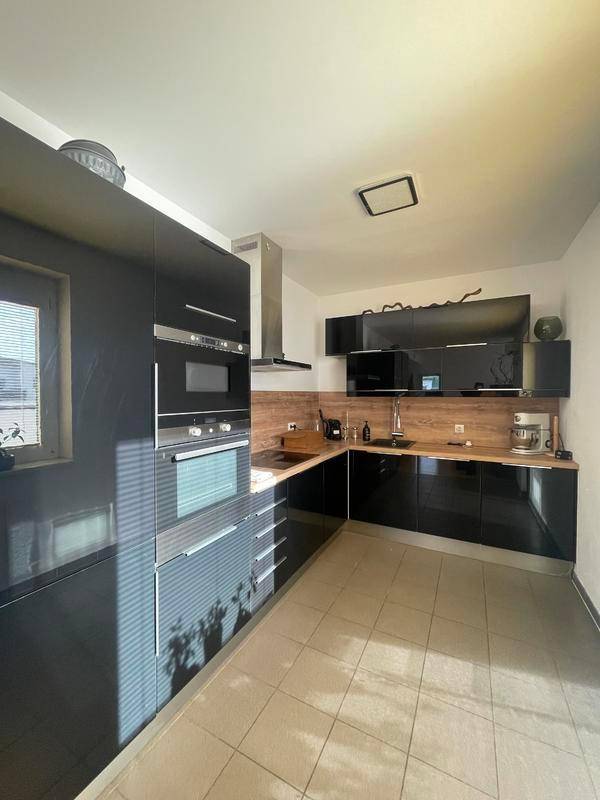 Moderne schwarze Einbauküche mit glänzenden Fronten, Holz-Arbeitsplatte und Fliesenboden.