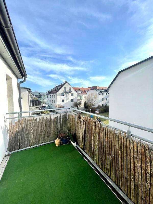 Balkon mit Kunstrasen und Sichtschutz, bietet einen Blick auf die umliegenden Gebäude.