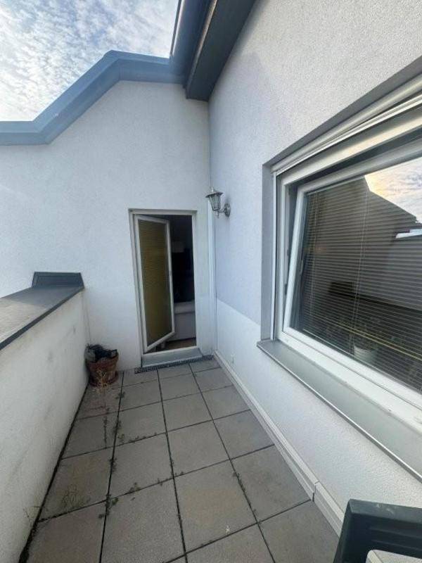 Kleiner gefliester Balkon mit offener Tür und Blick auf den Himmel.