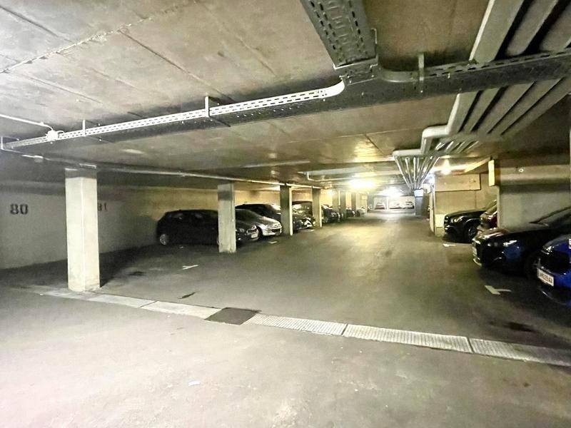 Tiefgarage mit mehreren geparkten Autos und sichtbaren Leitungen an der Decke.