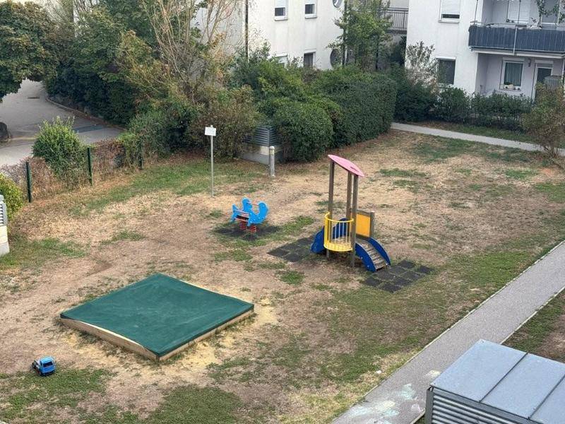 Spielplatz mit Sandkasten, Rutsche und Wippe in einer Wohnanlage.