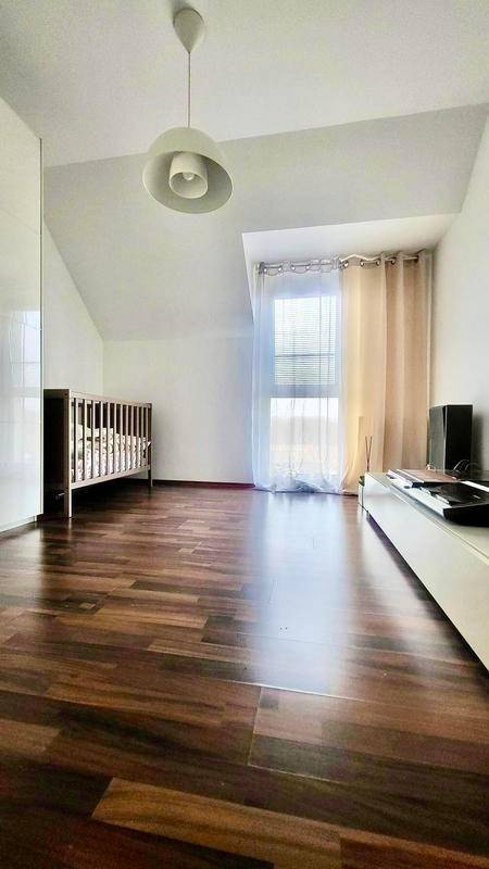 Helles Zimmer mit Holzboden, Kinderbett und Fenster mit Vorhängen.