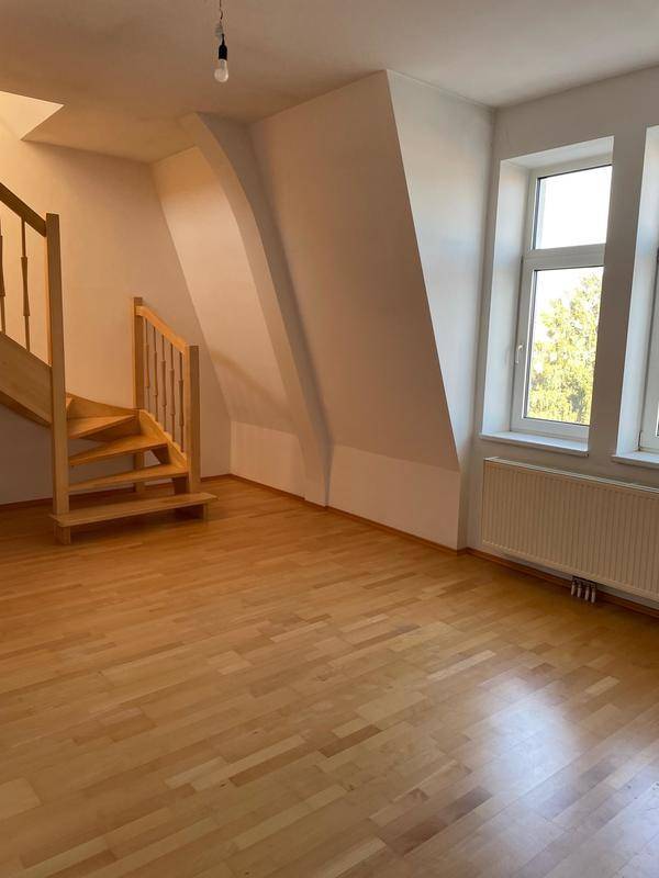 Geräumiger Wohnbereich mit Holztreppe, Dachschräge und großen Fenstern.
