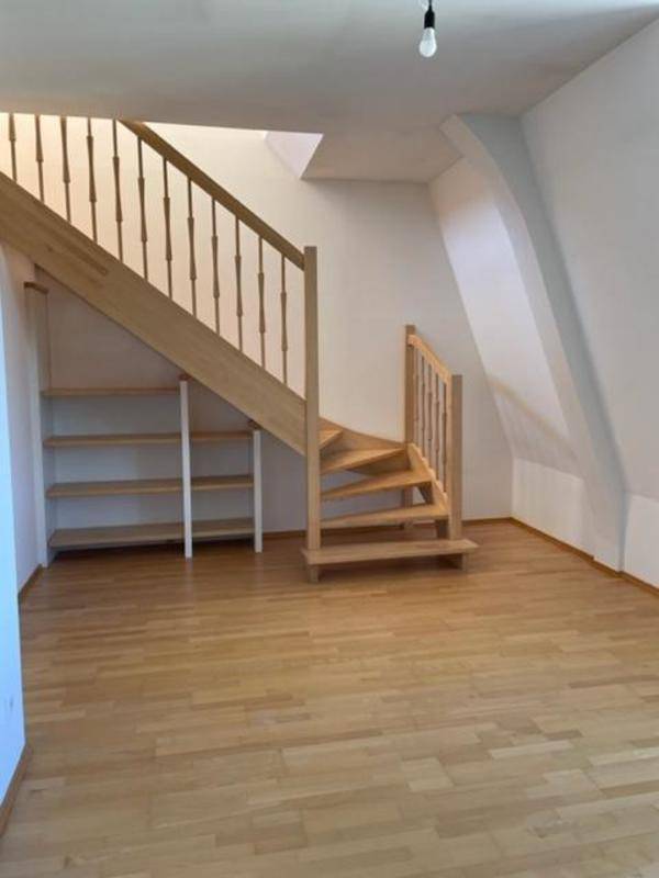 Heller Wohnbereich mit offener Holztreppe und integrierten Regalen unter der Treppe.