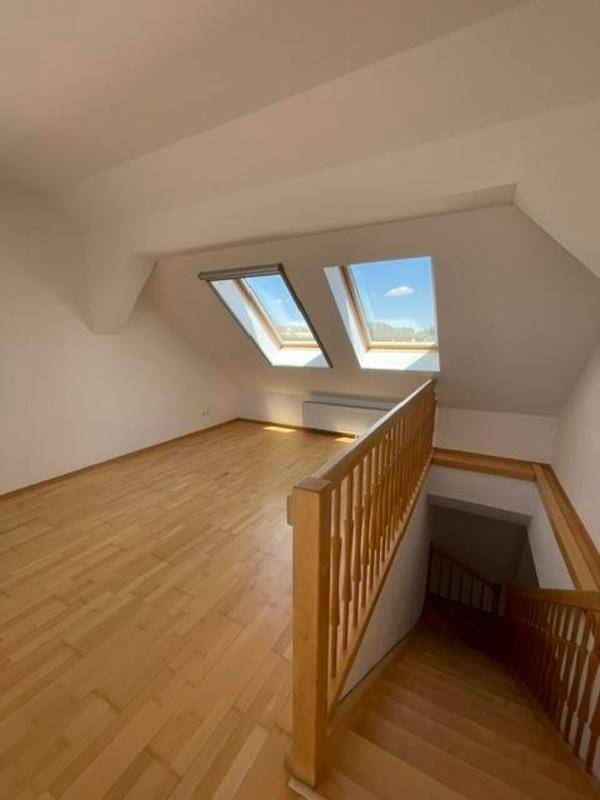 Offener Wohnbereich mit Holztreppe und zwei Dachfenstern, die den Raum erhellen.
