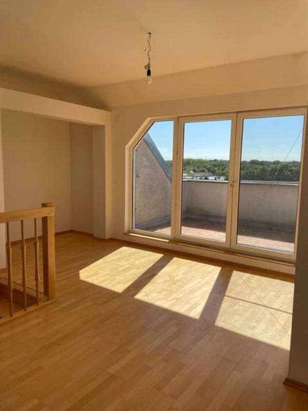Heller Raum mit Zugang zur Terrasse, Holzgeländer und Dachschräge.