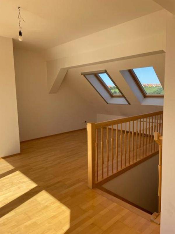 Offener Wohnbereich mit Holztreppe und zwei Dachfenstern, die viel Licht spenden.