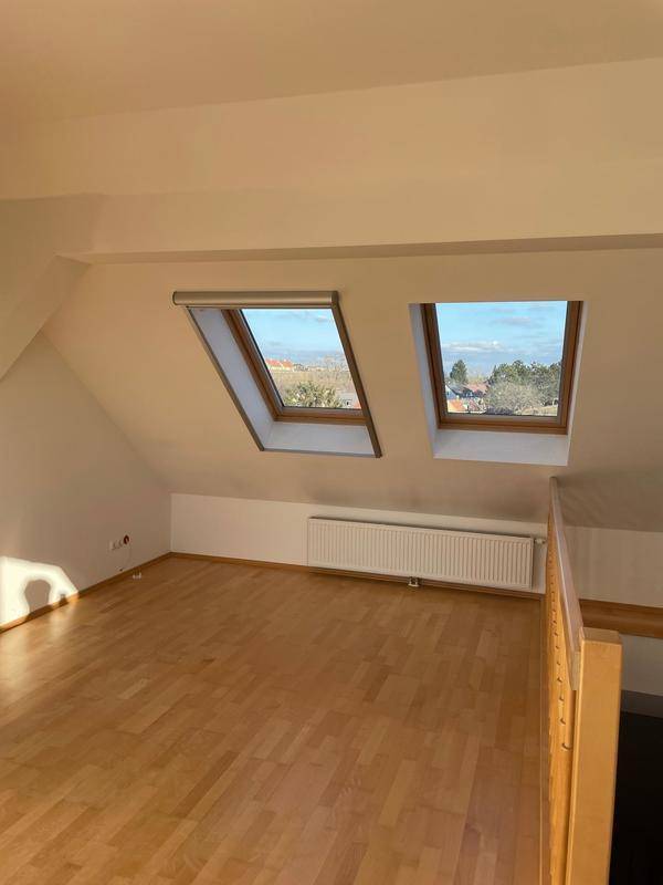 Helles Zimmer im Dachgeschoss mit zwei Dachfenstern und Holzboden.