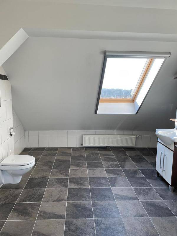 Helles Badezimmer mit wandhängendem WC, Waschbecken und Dachfenster.