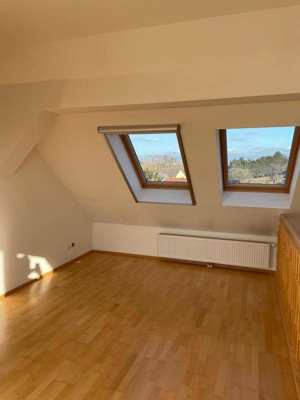 Helles Dachzimmer mit zwei Dachfenstern und Heizkörper, ideal als Schlafzimmer.