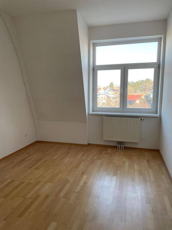 Helles Schlafzimmer mit Dachschräge, Fenster und Heizkörper.