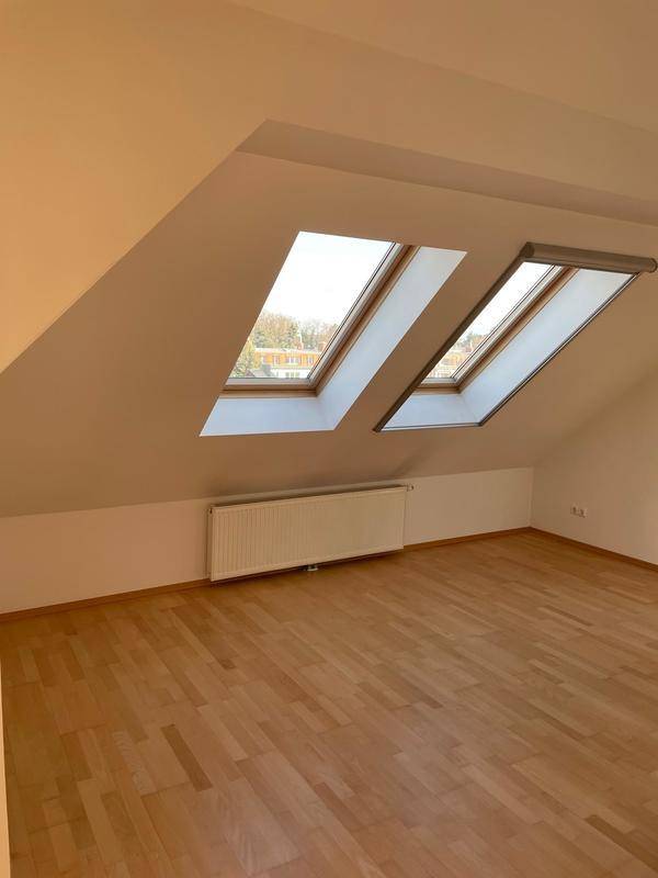 Geräumiges Dachzimmer mit zwei Dachfenstern und hellem Parkettboden.