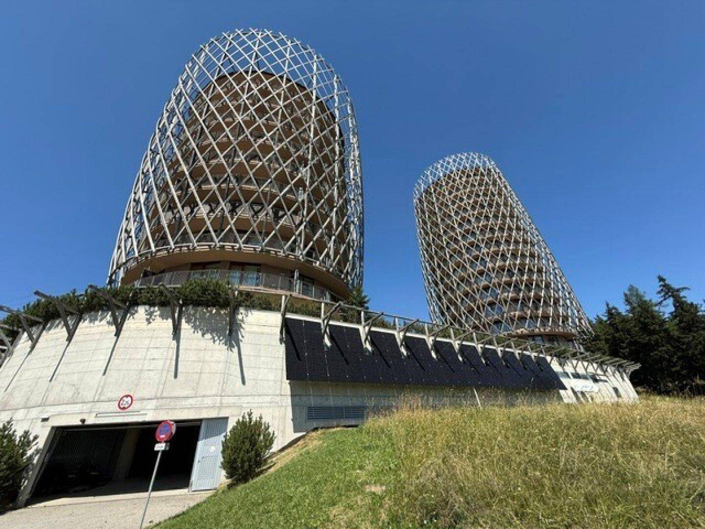 Moderne Architektur der zylindrischen Gebäude mit Gitterfassade und Tiefgaragenzufahrt an einem sonnigen Tag.