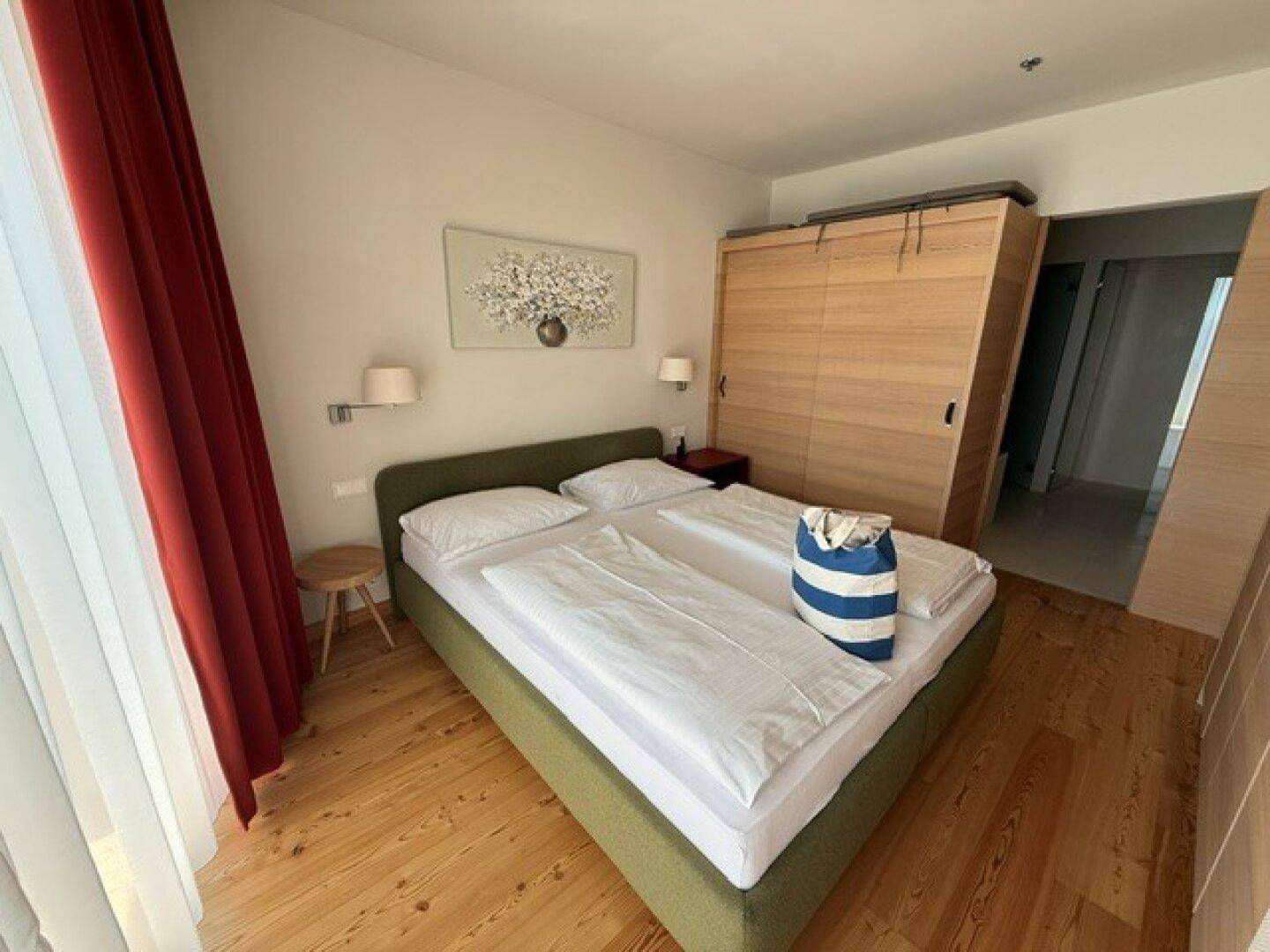 Helles Schlafzimmer mit Doppelbett, Holzboden und praktischen Einbauschränken für ausreichend Stauraum.