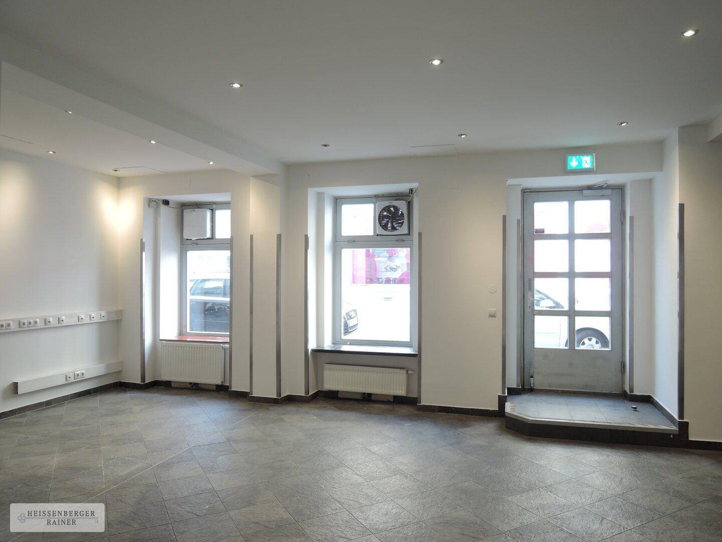 Heller, leerer Geschäftsraum mit großen Fenstern, Fliesenboden und direktem Straßenzugang.