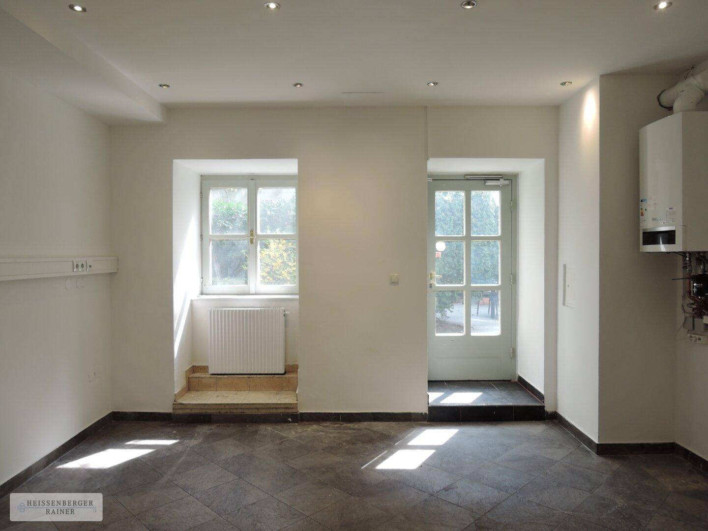 Leerer Geschäftsraum mit Fenster, Tür und sichtbarem Heizkessel an der Wand.