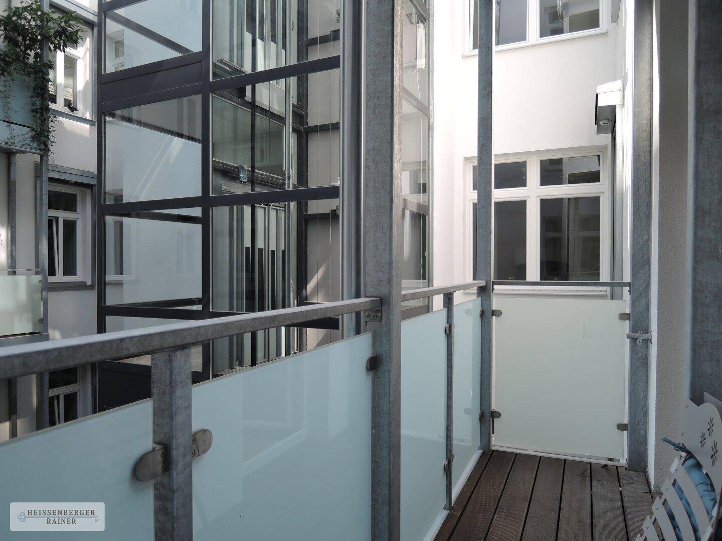 Balkon mit Holzboden und Blick auf den gläsernen Aufzug im Innenhof des Gebäudes.
