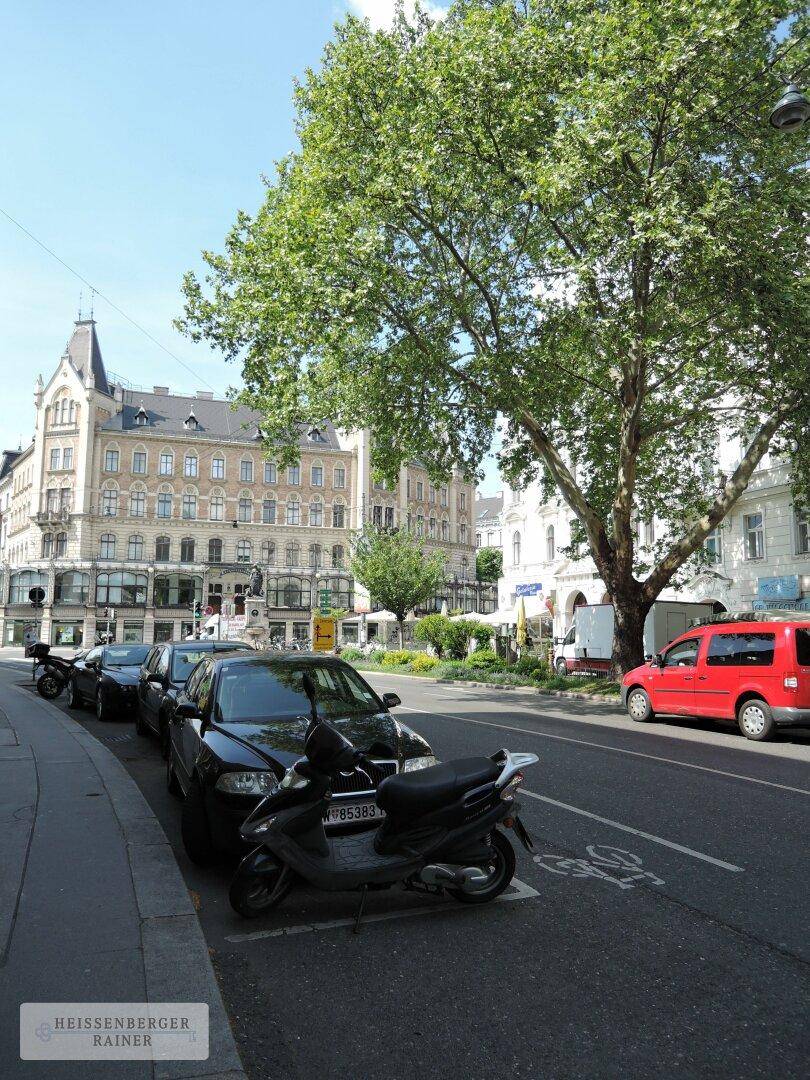Stadtansicht mit geparkten Autos, Bäumen und historischen Gebäuden, belebte Umgebung.