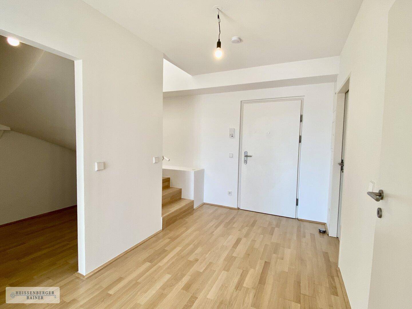 Eingangsbereich mit Holzboden, weißer Tür und Zugang zur oberen Etage über eine Treppe.