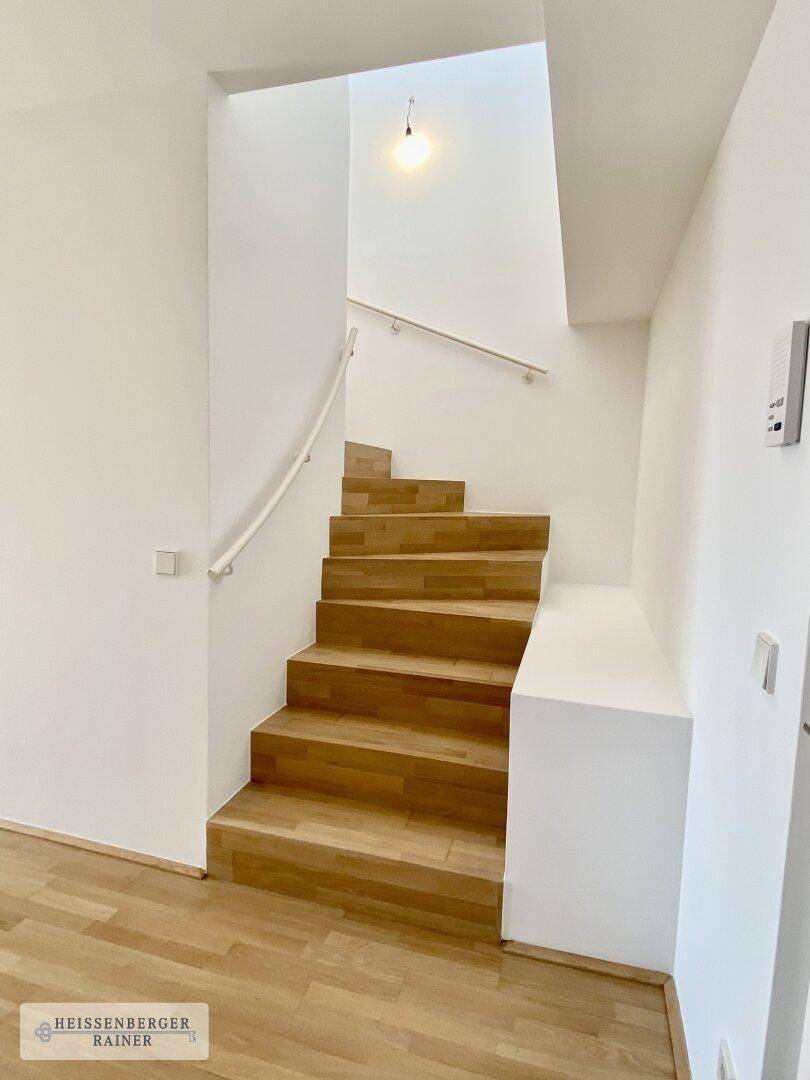 Moderne Holztreppe mit schlichtem Geländer in einem hellen Treppenhaus.