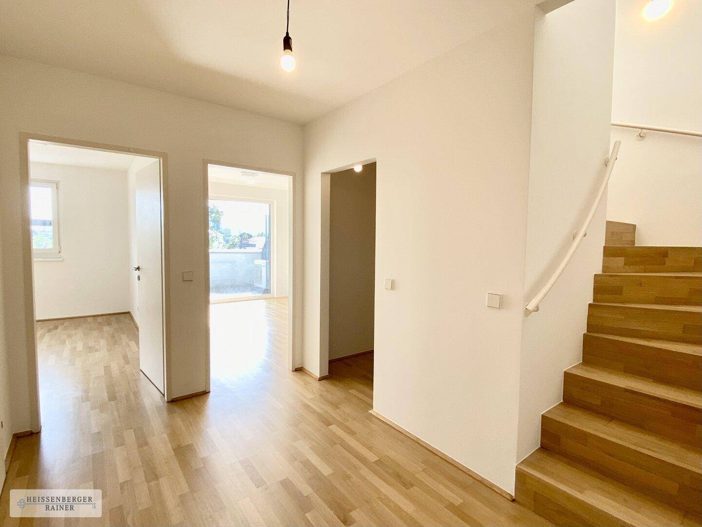 Heller Flur mit Holzboden, der zu verschiedenen Räumen und einer Treppe führt.