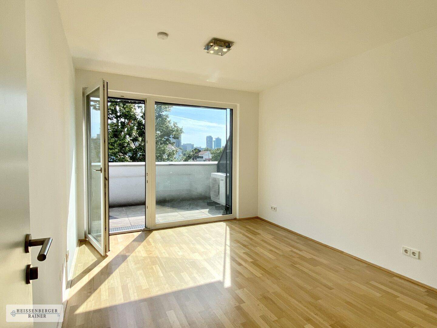 Leeres Zimmer mit Holzboden und direktem Zugang zu einem kleinen Balkon.