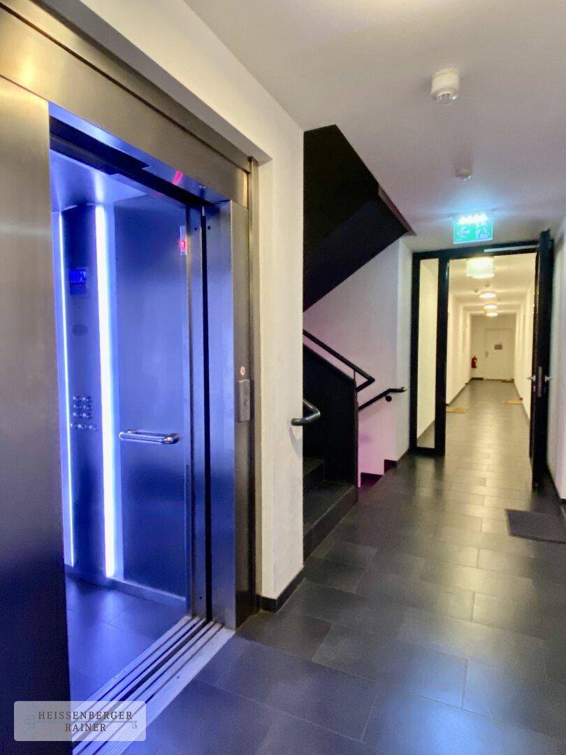 Moderner Flur mit Aufzug und Treppenhaus, beleuchtet mit blauen Akzenten.