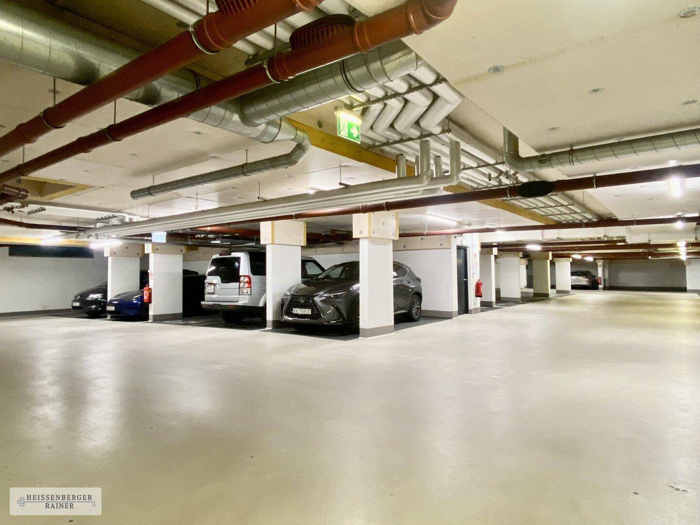 Geräumige Tiefgarage mit mehreren Stellplätzen und sichtbaren Installationen an der Decke.