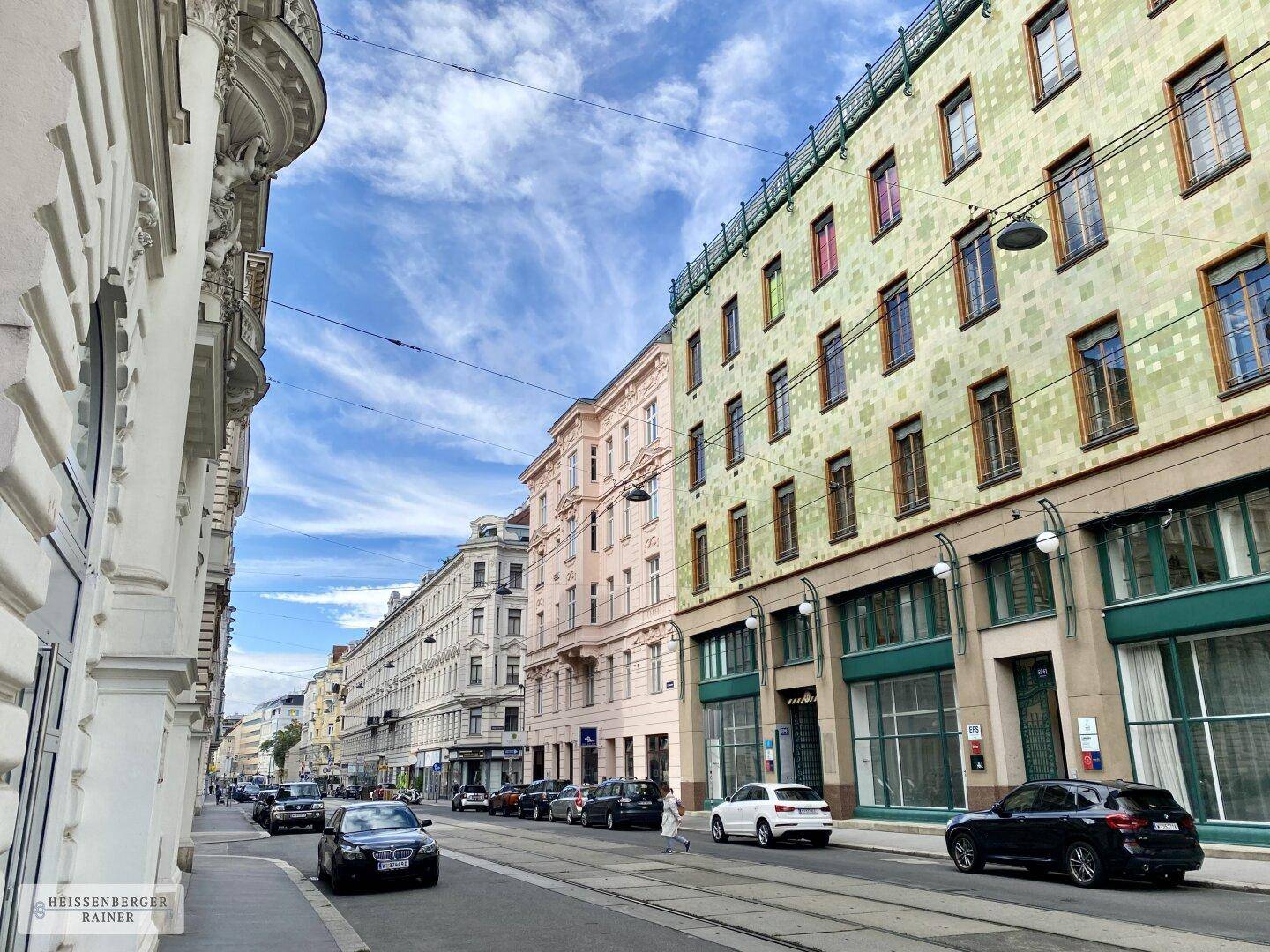 Weitläufige Straßenansicht mit historischen Gebäuden, darunter das markante grüne Haus, und parkenden Autos.