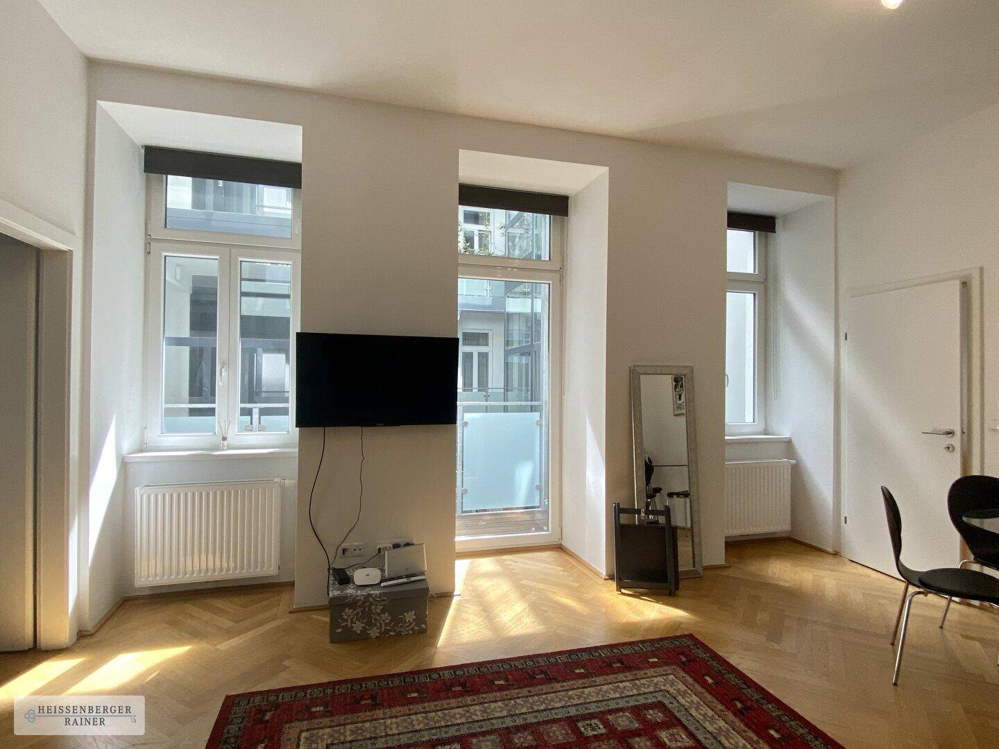 Lichtdurchflutetes Wohnzimmer mit Fischgrätparkett und französischem Balkon, der viel Tageslicht bietet.
