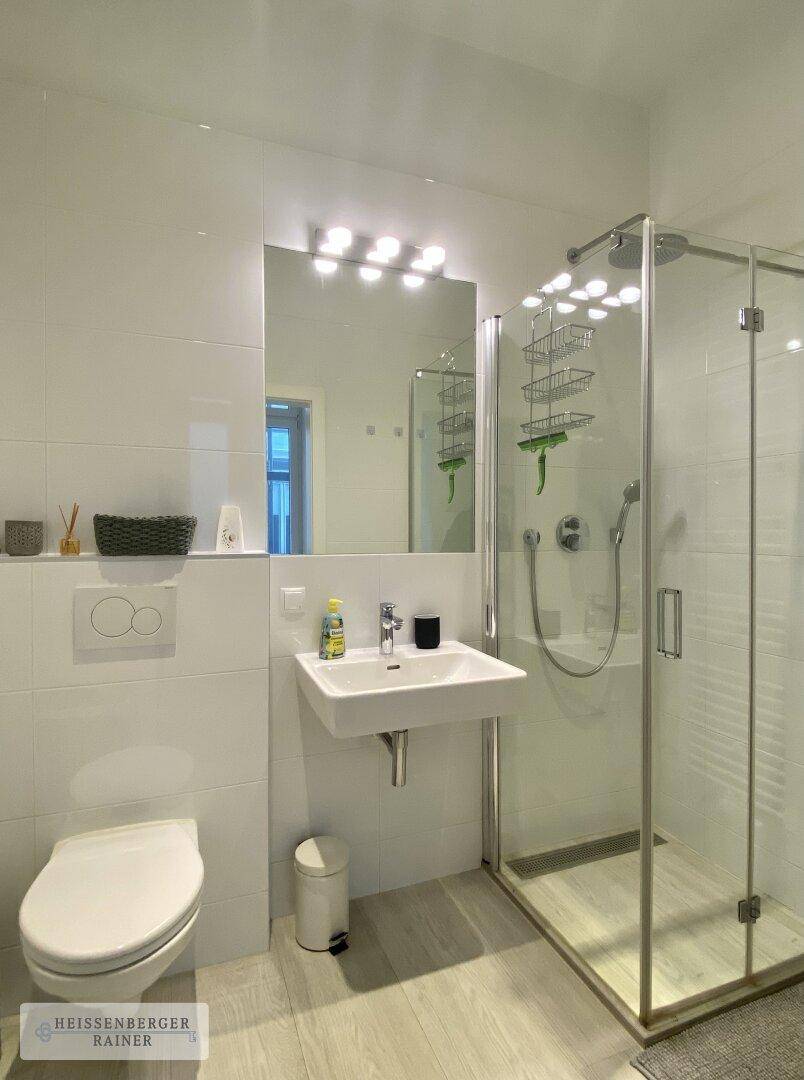 Modernes Badezimmer mit ebenerdiger Dusche, WC und Waschbecken, in hellen Fliesen gehalten.