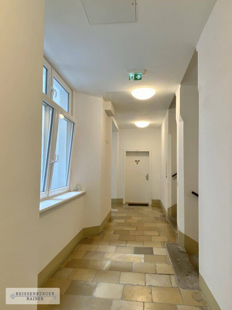 Gemeinschaftlicher Flur im Gebäude mit Fliesenboden und Fenstern, gut beleuchtet.