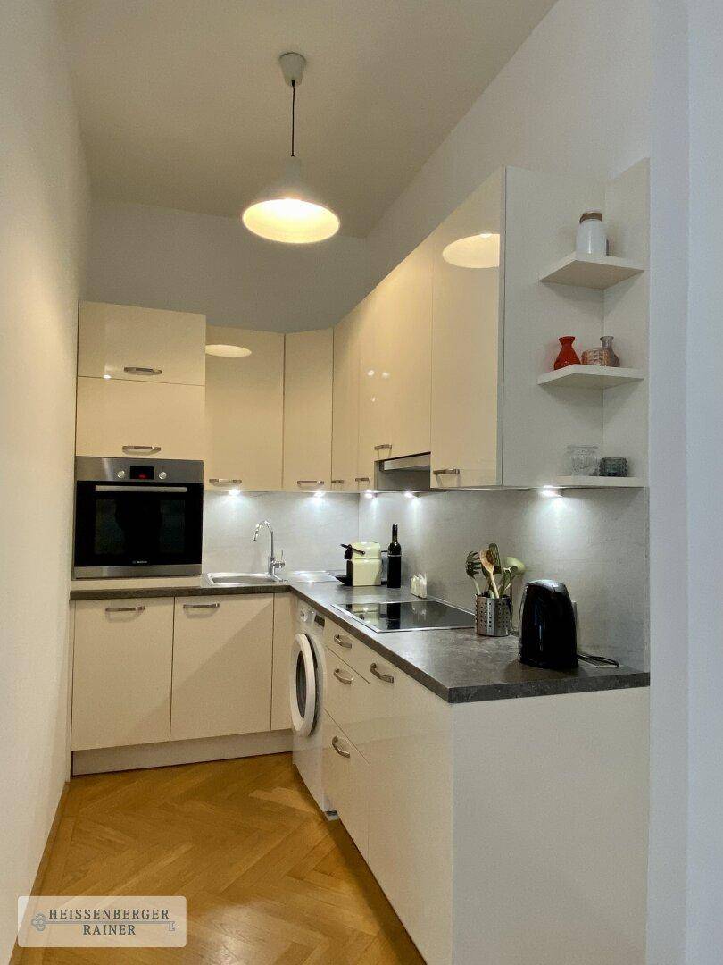 Moderne Einbauküche mit weißen Hochglanzfronten und integrierten Geräten für effizientes Kochen.