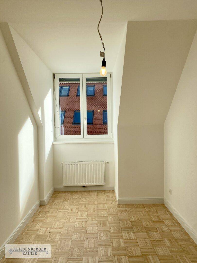 Kleines, helles Zimmer im Dachgeschoss mit Parkettboden, Schrägen und Fenster.