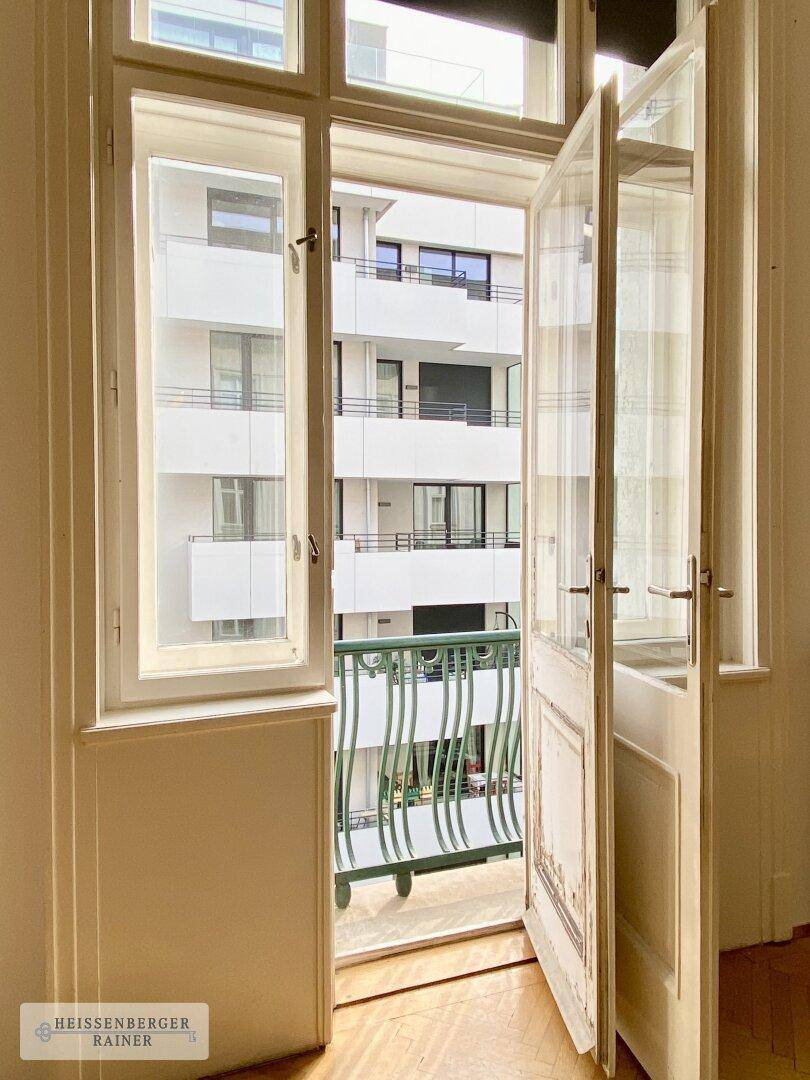 Blick durch eine offene Balkontür auf ein gegenüberliegendes modernes Gebäude und einen kleinen Balkon.