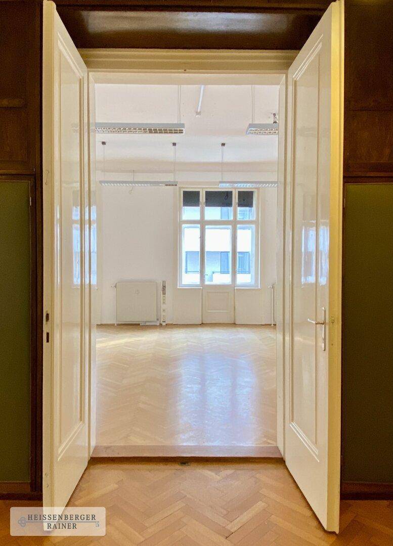 Blick durch eine weit geöffnete Doppeltür in einen hellen Büroraum mit Parkettboden.