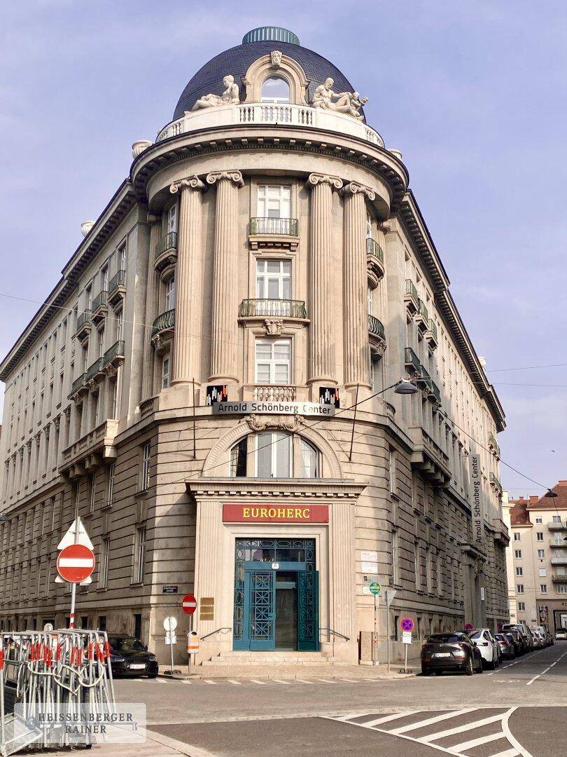 Historisches Eckgebäude mit Kuppel, Säulen und klassischer Fassade an einer belebten Straße.