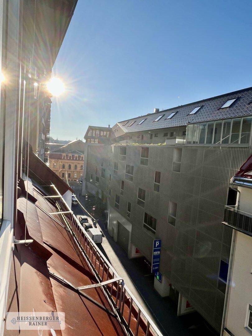 Sonniger Blick von oben auf eine städtische Straße mit Gebäuden und parkenden Fahrzeugen.