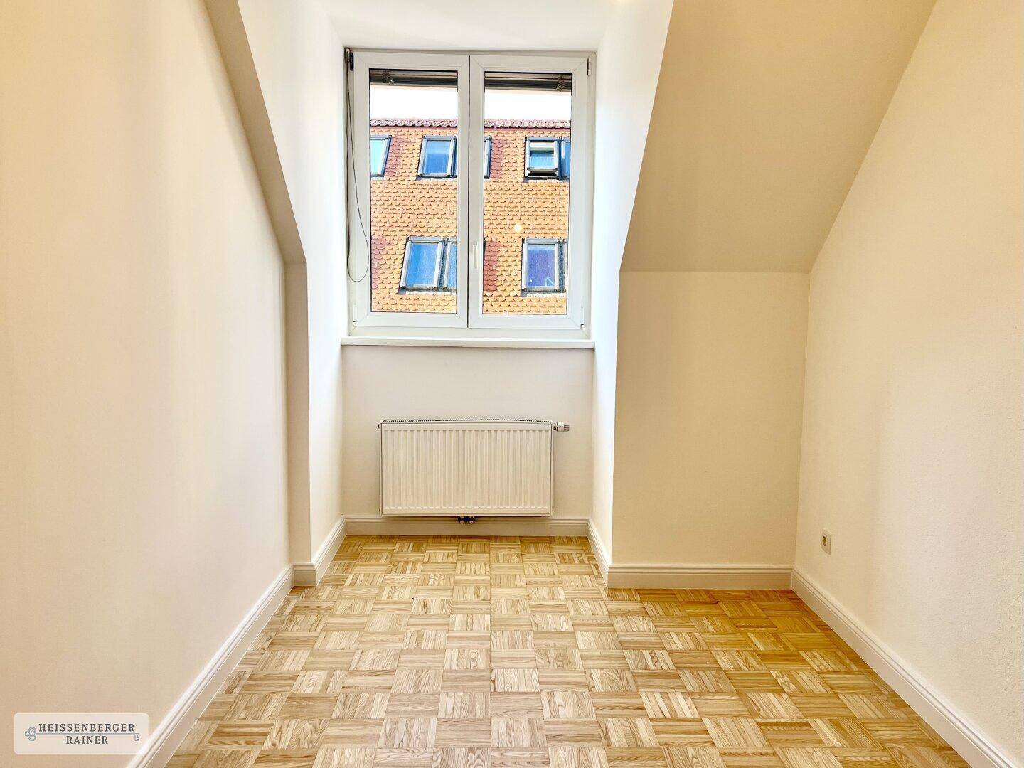 Helles Dachgeschosszimmer mit Parkettboden, schrägen Wänden und einem großen Fenster.