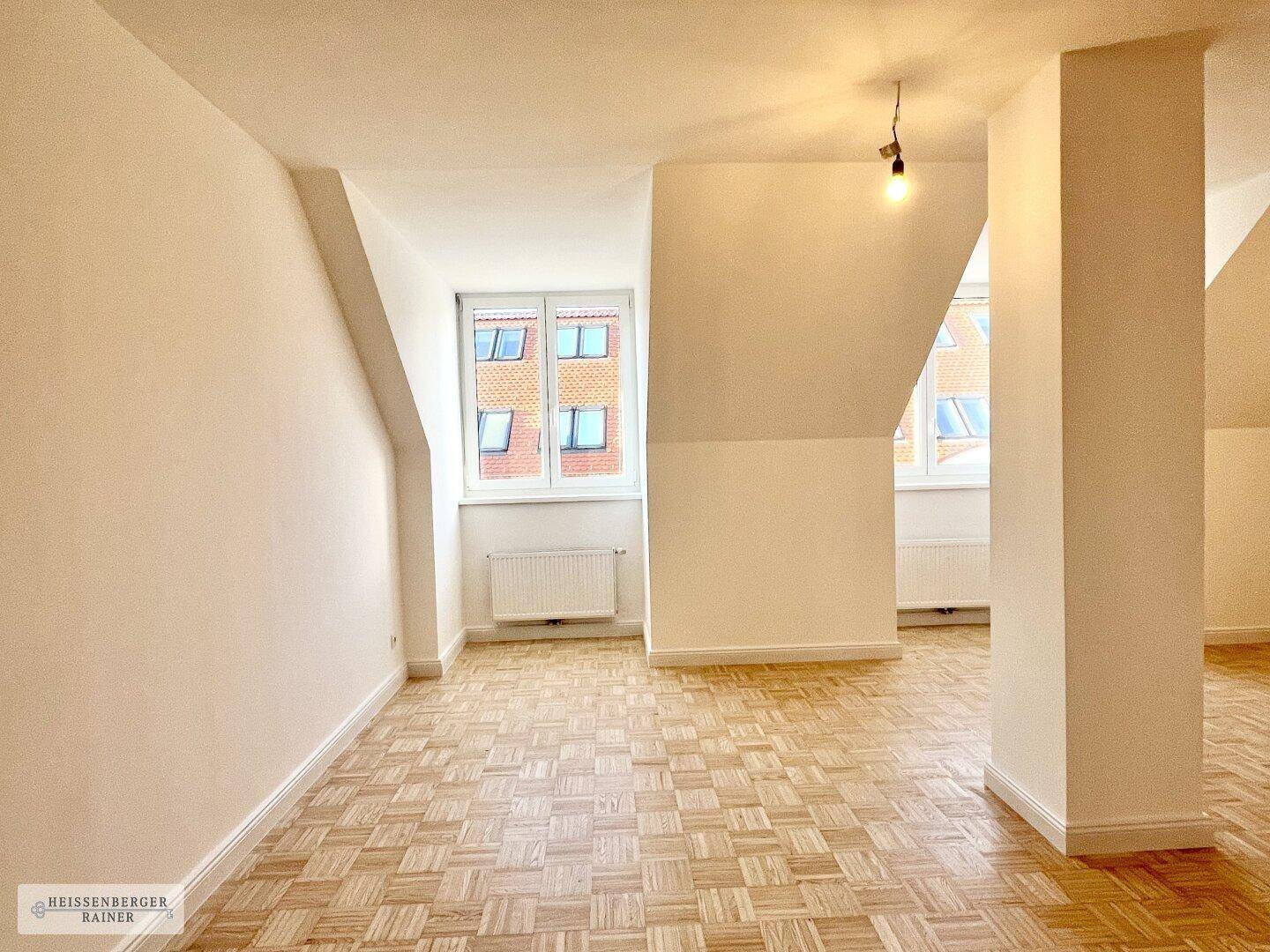 Geräumiges Dachgeschosszimmer mit Parkettboden, schrägen Wänden und zwei Fenstern.
