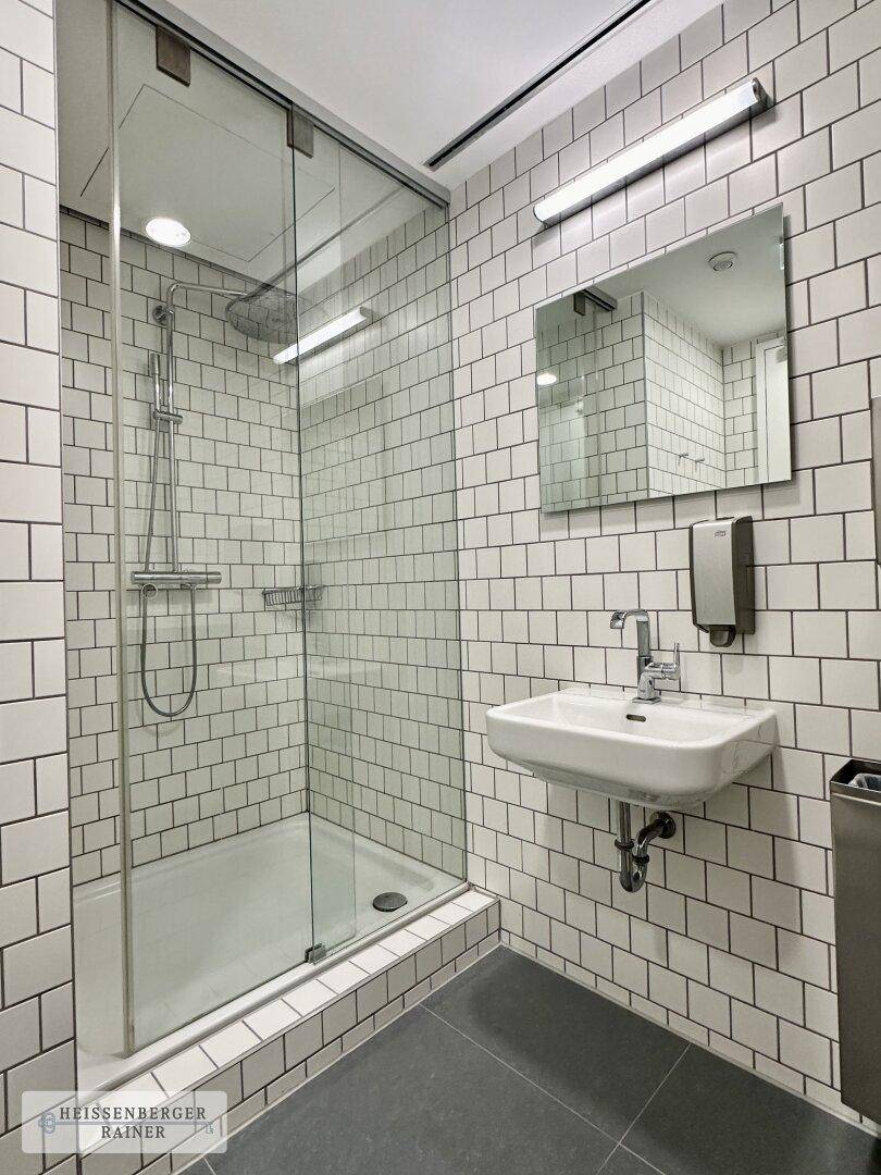 Modernes Badezimmer mit weiß gefliesten Wänden, ebenerdiger Dusche und Hänge-Waschbecken.