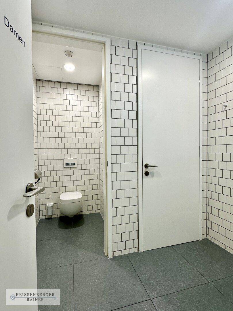 Sauberer Toilettenbereich mit weißen Metro-Fliesen, Hänge-WC und dunklem Fliesenboden.