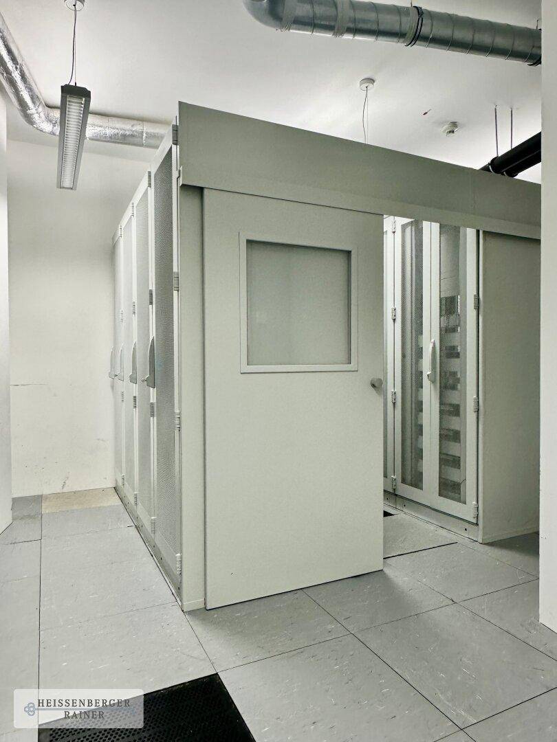 Technischer Raum mit Serverschränken, Fliesenboden und sichtbaren Lüftungsrohren.